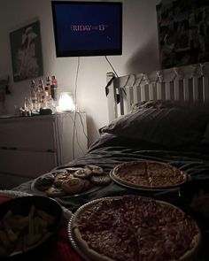 three pizzas are sitting on the bed in front of a flat screen tv that is turned on