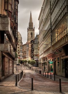 an empty city street with tall buildings on both sides and a clock tower in the background