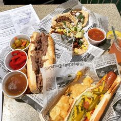 a table topped with two hot dogs covered in toppings next to bowls of condiments