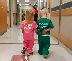 two children in pink and green scrub suits walking down a hospital hallway with their doctor training shirts on