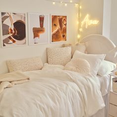 a bed with white sheets and pillows in a bedroom next to pictures on the wall