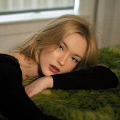 a woman laying on top of a green rug in front of a window with her arms crossed