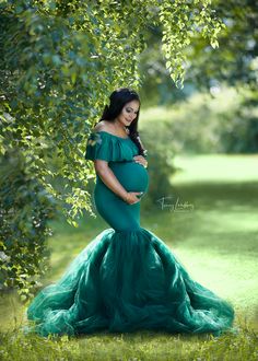 a pregnant woman in a green gown standing under a tree with her belly tucked up