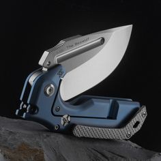 a blue folding pocket knife on top of a rock with the blade still attached to it