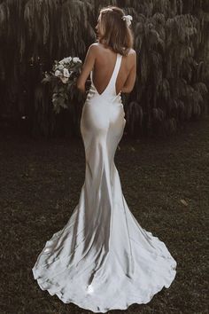 the back of a woman in a white dress standing on grass with trees behind her