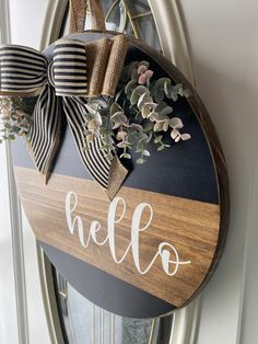 a wooden sign with the word hello painted on it and a bow hanging from it's front door