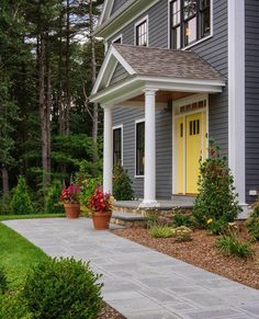 a yellow door is on the side of a gray house with white columns and pillars