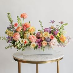 an arrangement of colorful flowers in a white vase on a marble table with gold legs