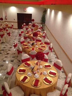 a banquet hall with tables and chairs covered in red and white linens, gold plates and napkins