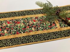 a table runner with pine cones and red berries on black fabric, next to a potted plant