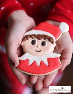 a close up of a person holding a cookie in their hands with a santa clause hat on