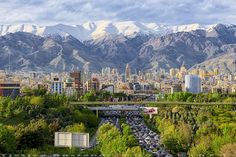 a city with mountains in the background and cars driving on it's road below