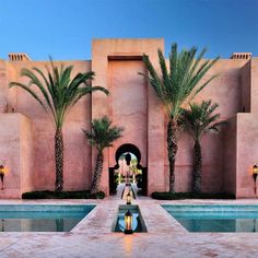 an outdoor swimming pool with palm trees in the foreground and a building behind it