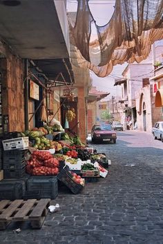 an outdoor market with fruits and vegetables on the side walk in front of a building