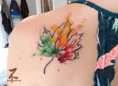 a woman's back with a colorful leaf tattoo on it