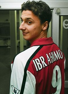 a man in a red and white jersey standing next to an open door with his hand on his hip