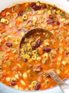 a ladle full of soup with pasta and beans in it, ready to be eaten