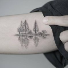 a woman's arm with trees on it and water in the foregrounds