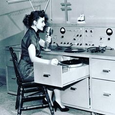 a woman sitting at a desk with a record player in front of her, holding a microphone