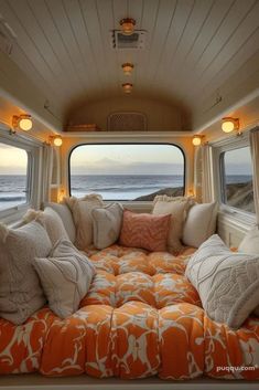 an orange and white couch sitting in front of a window next to the ocean with lots of pillows on it