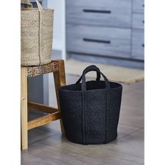 a black basket sitting on the floor next to a wooden chair with a bag in front of it