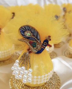 several small yellow vases with pearls and peacock decorations on top of white table cloth