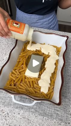 a person pouring sauce on some pasta in a dish with other food items around it