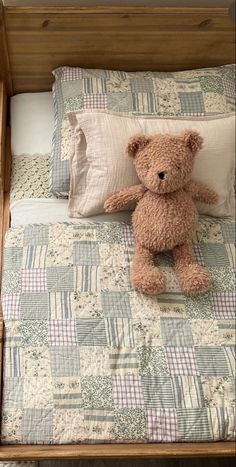 a brown teddy bear sitting on top of a bed next to pillows and pillow cases