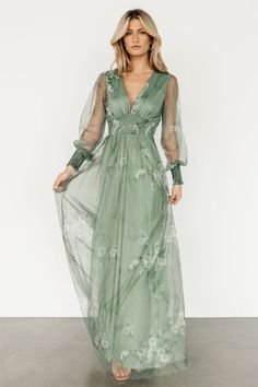 a woman in a long green dress with sheer sleeves and flowers on the waist,