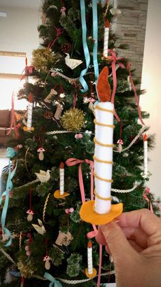 a person is holding a candle in front of a christmas tree with ribbons on it