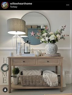 a wooden table topped with a vase filled with flowers next to a mirror and lamp