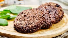 two cookies are on a wooden plate with some green leaves next to it and a glass of tea in the background