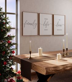 a wooden table with candles on it in front of two framed pictures and a christmas tree