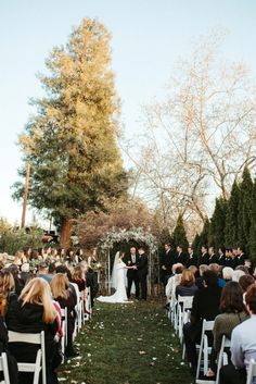 an outdoor wedding ceremony with people sitting in chairs watching the bride and groom walk down the aisle