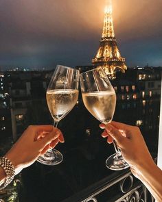 two people toasting wine glasses in front of the eiffel tower at night