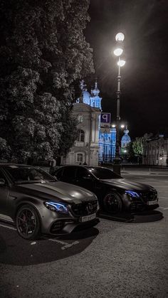 two cars parked next to each other in front of a tall building at night time