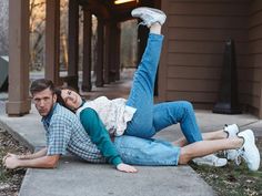 a man and woman laying on the ground in front of a house with their arms around each other