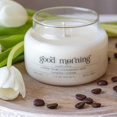 a white candle sitting on top of a wooden table next to some flowers and coffee beans