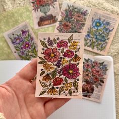 a hand holding four small cards with flowers on them