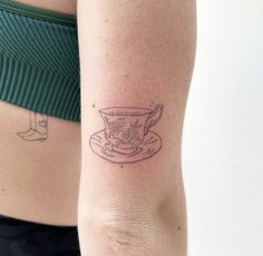 a woman with a tattoo on her arm has a cup and saucer in front of her