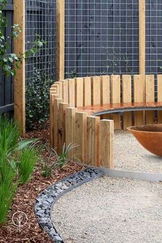 a wooden bench sitting in the middle of a gravel area next to a tree and fence