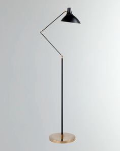 a black and gold floor lamp on a white surface with a round base, the light is turned on