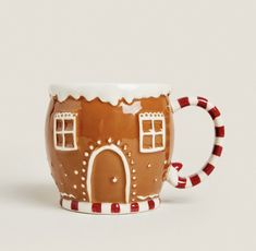 a ceramic mug with a gingerbread house on it's side and candy canes around the rim