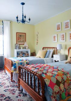 two beds in a room with yellow walls and pictures on the wall above them,