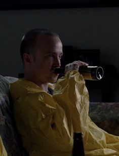 a man in a yellow raincoat drinking from a beer bottle while sitting on a couch