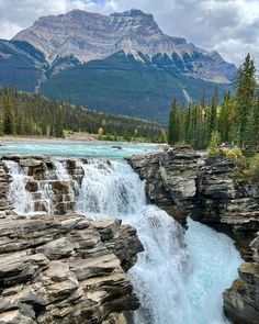 the water is rushing over the rocks near the trees and mountain range in the background