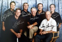 a group of men posing for a photo in front of a blue backdrop with the names of their coaches