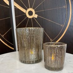 two silver glass cups sitting on top of a white marble table next to a bicycle wheel