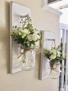 two mason jars with flowers are hung on the wall