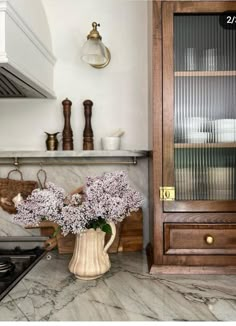 a vase filled with purple flowers sitting on top of a counter next to a stove